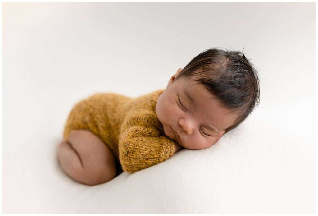 studio vs lifestyle newborn photography- this is an example of posed newborn baby girl wearing a yellow knit outfit in the Glean & Co studio 