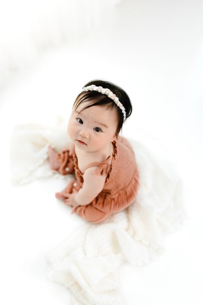 8 month old milestone photography session for baby girl in coral jumpsuit sitting up on simple clean white background. One of 12 Baby Milestone Photography Ideas