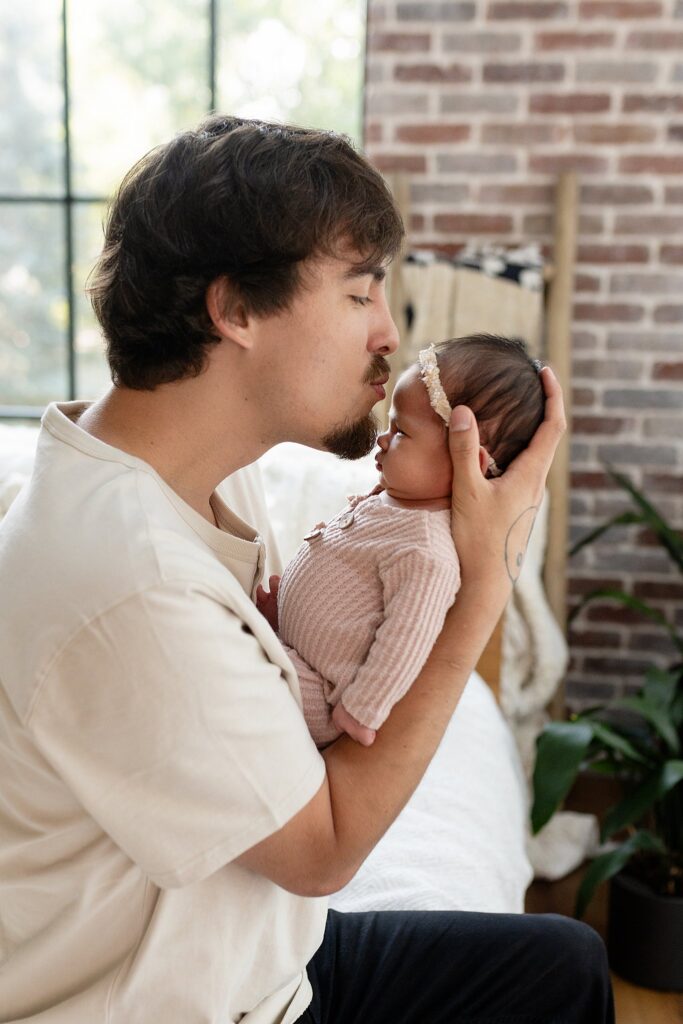 a new dad kissing his newborn baby daughter